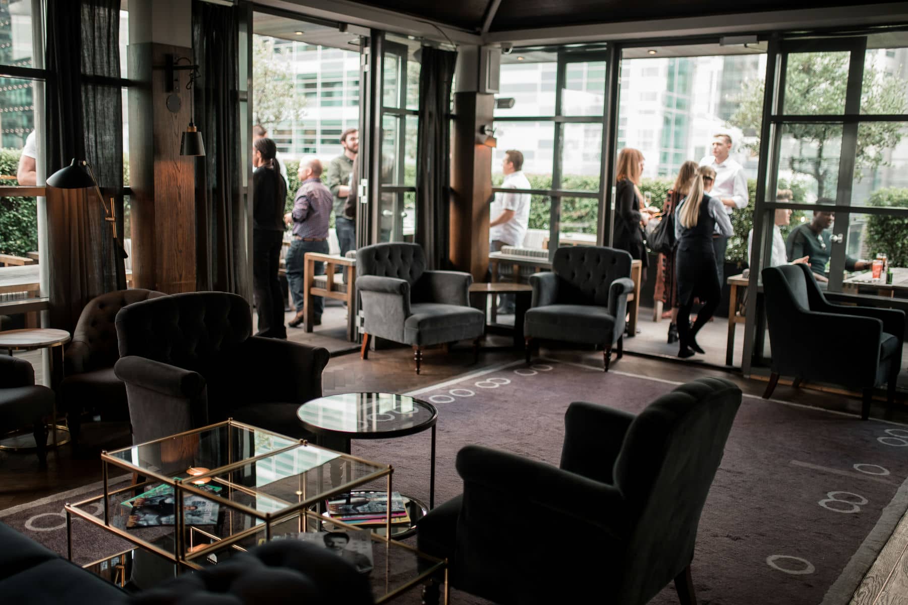 Guests talking in a dark, comfortable lounge at Eight Moorgate, with armchairs and tall windows over the City